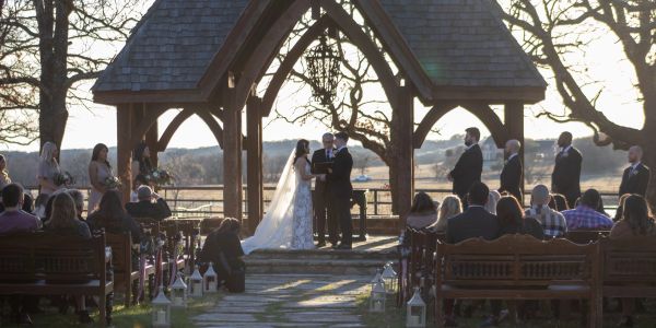 Outdoor wedding ceremony under wooden arch with guests seated.