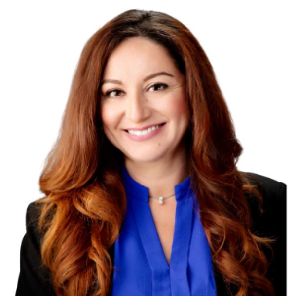 Smiling woman with long red hair in blue blouse and black blazer.