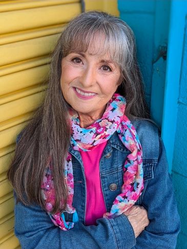 Smiling elderly woman in denim jacket and colorful scarf against vibrant background.