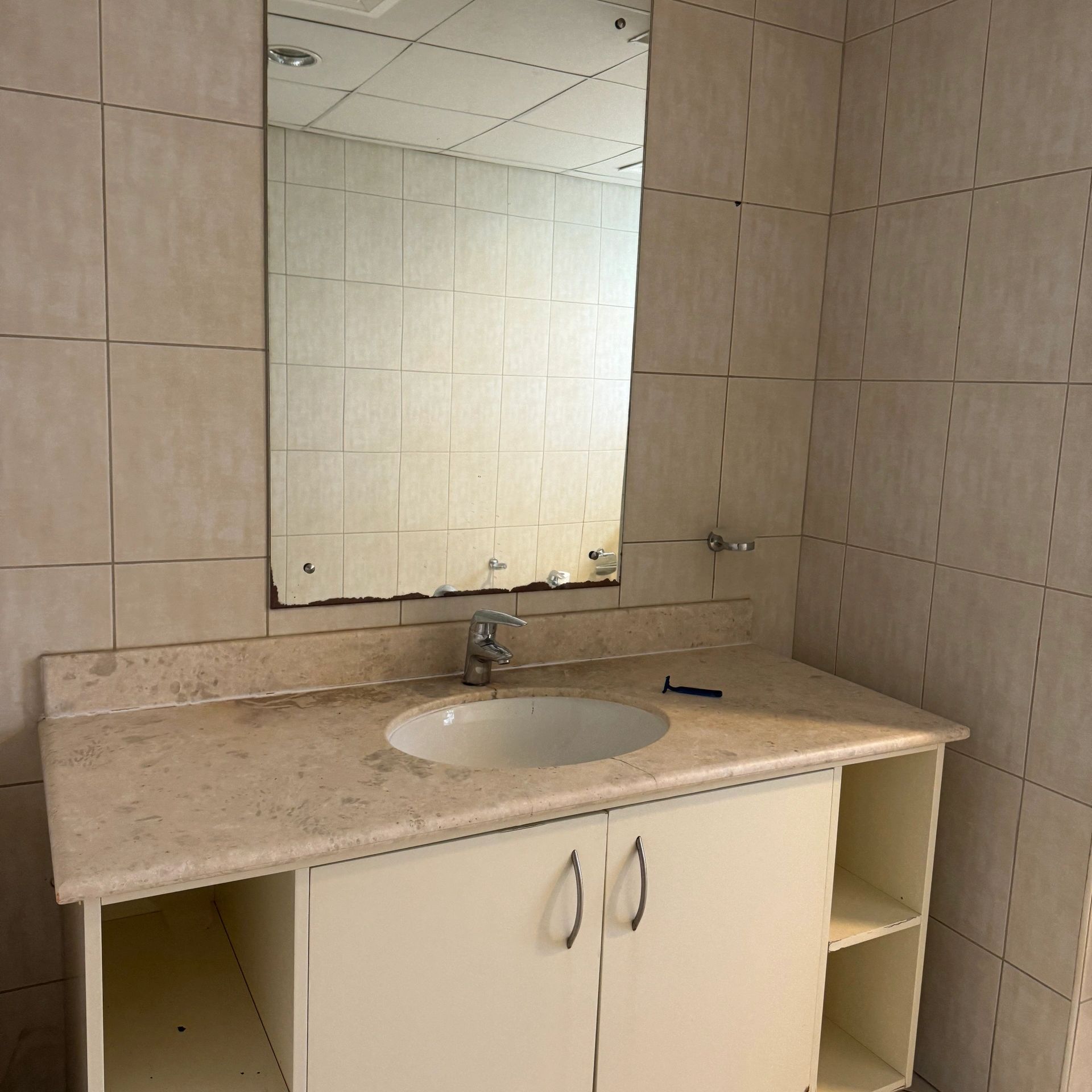Bathroom sink with a worn mirror and razor on counter.
