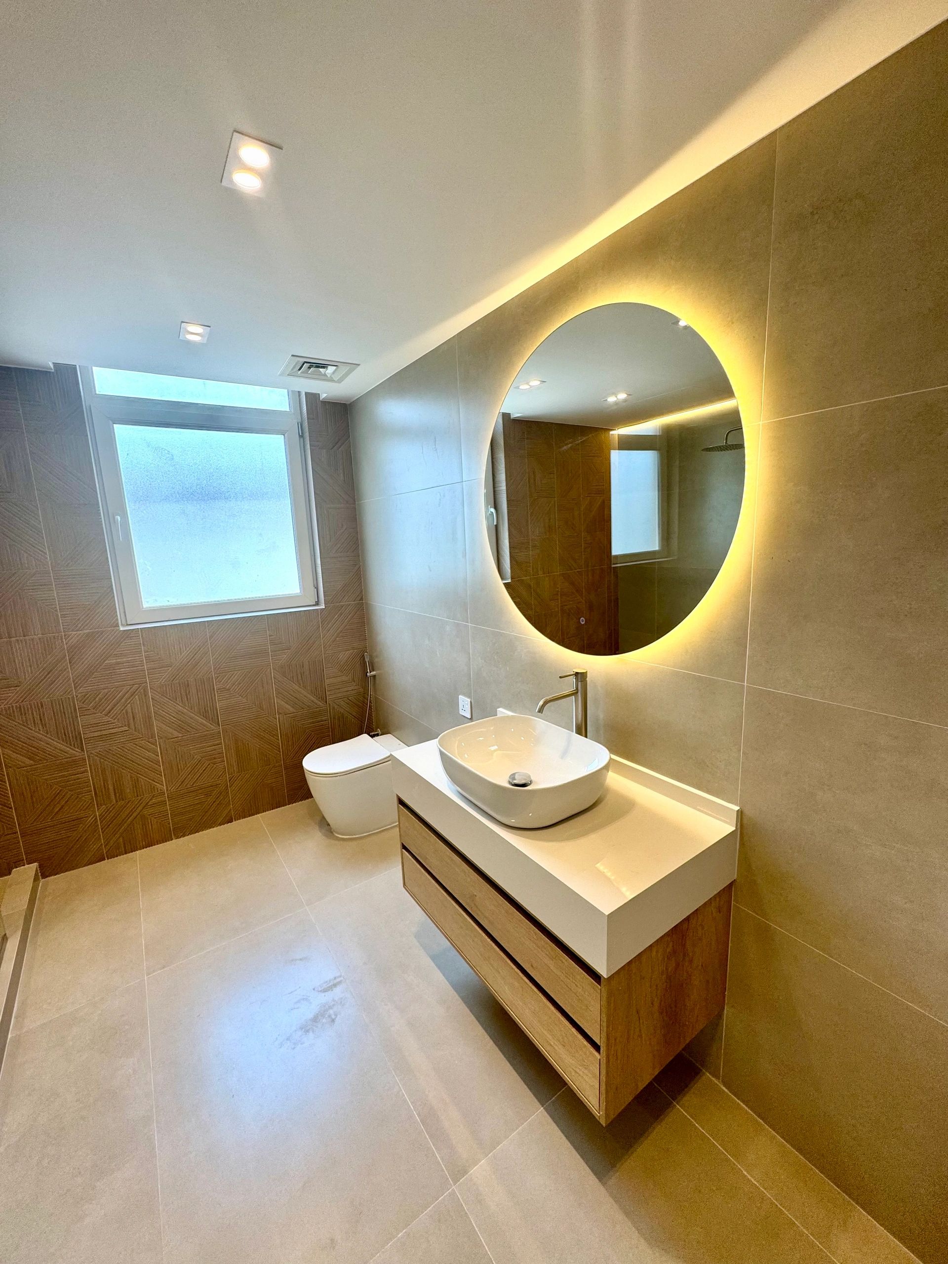 Modern bathroom with illuminated round mirror and wooden accents.