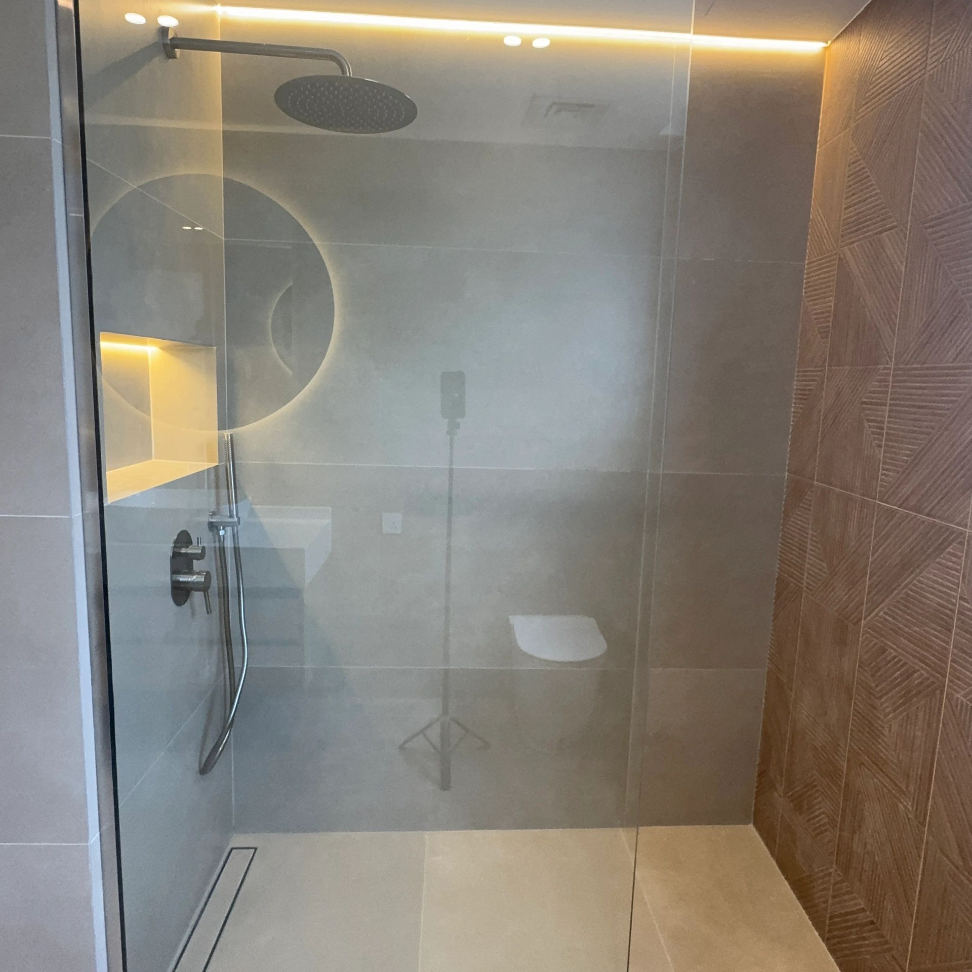 Modern glass shower with rain showerhead and ambient lighting.