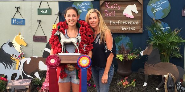 Two women celebrate winning with a horse trophy and ribbons at Kelly Bell Performance Horses display.