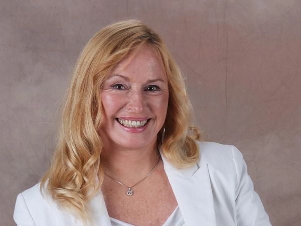 Barbara Ann Brennan, a woman with blond hair, smiling, wearing a white suit jacket.