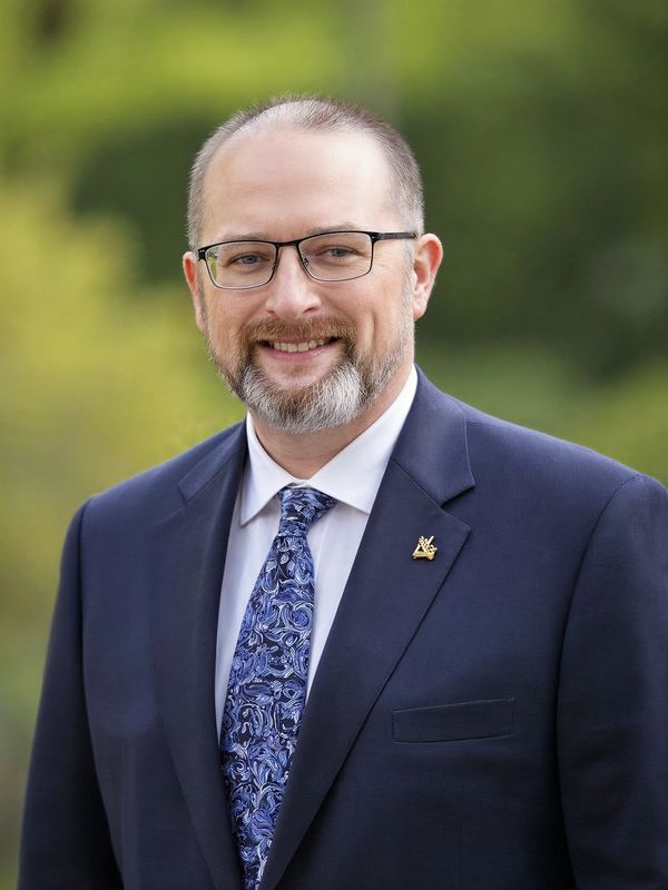 A smiling man in a suit and patterned tie outdoors.