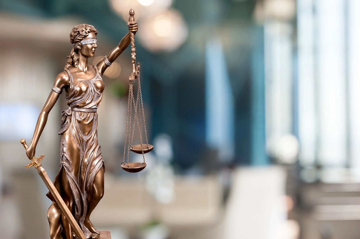 Bronze Scales of Justice Statue, the goddess Themis, hold scales and sword. Blurred background.