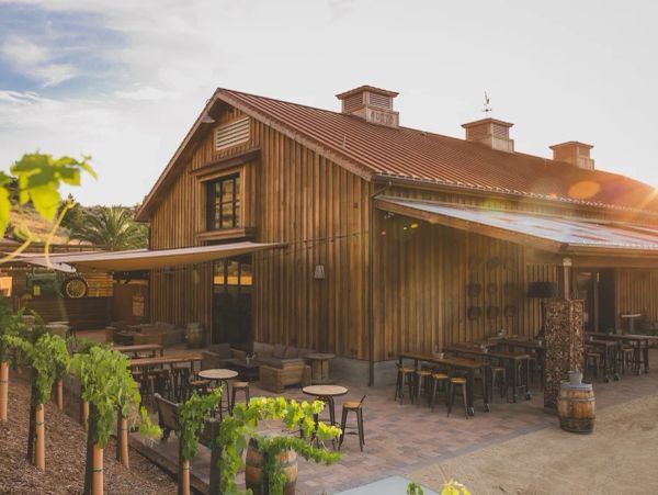 Rustic wooden winery building with outdoor seating at sunset.