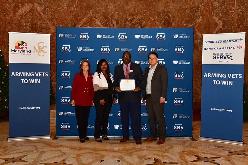 Four professionals pose with an award at a veterans' event.