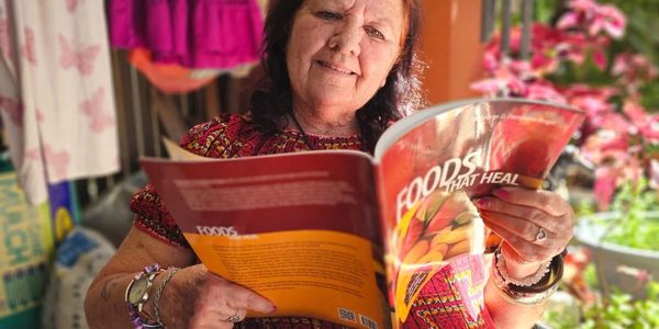 A woman reads a magazine titled 'Foods That Heal' with a smile.