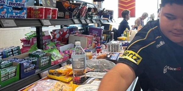 Young man at a grocery checkout with various snacks and drinks.