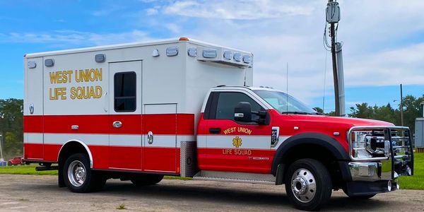 Red and white West Union Life Squad emergency vehicle parked outdoors.