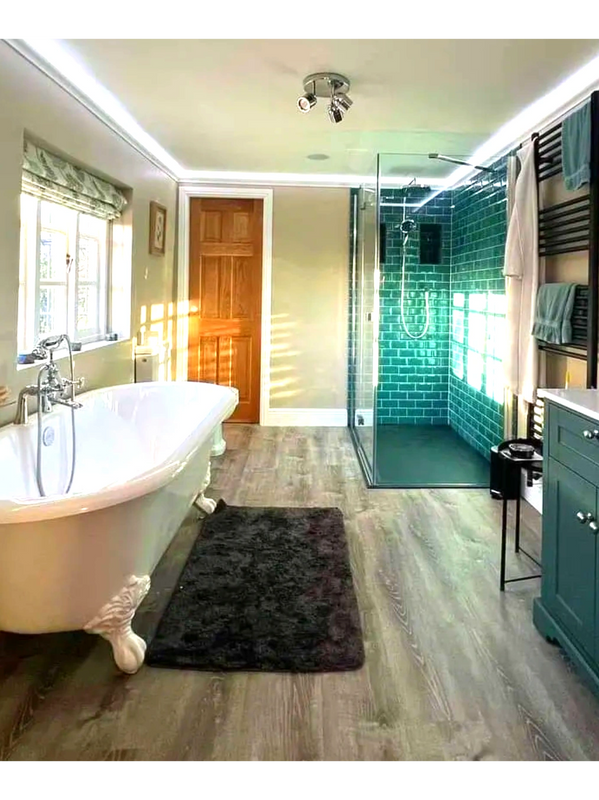 A clean Bathroom including a roll top bath and shower lit by sunlight 