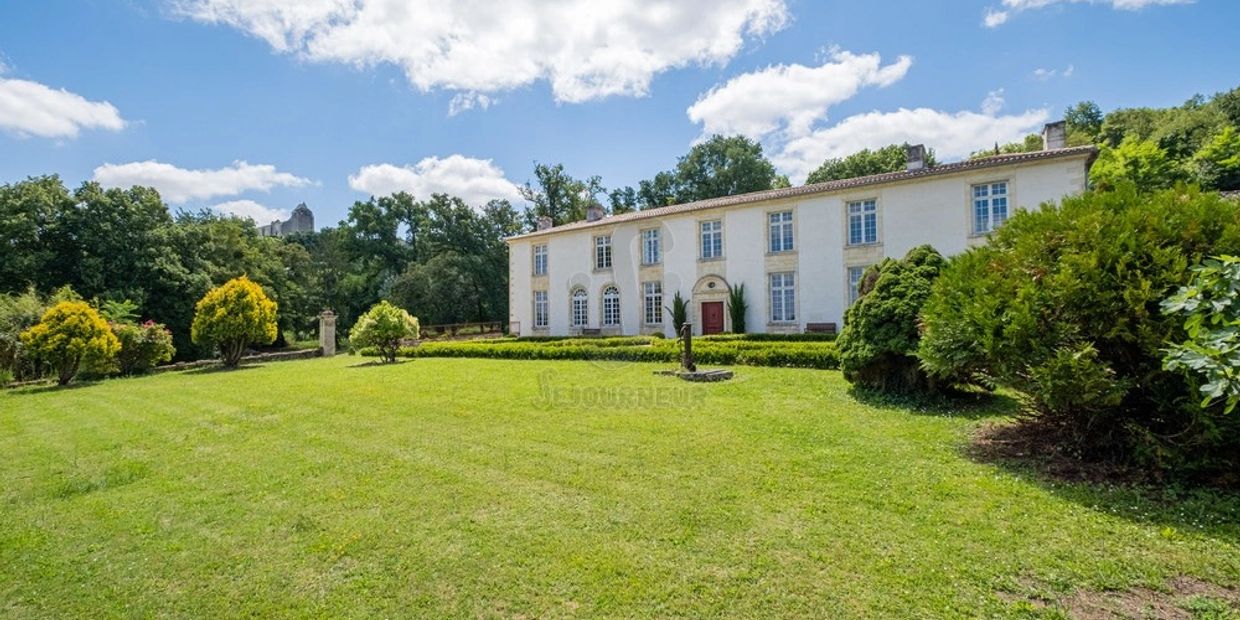 Large white mansion with manicured lawn and surrounding greenery under a blue sky.