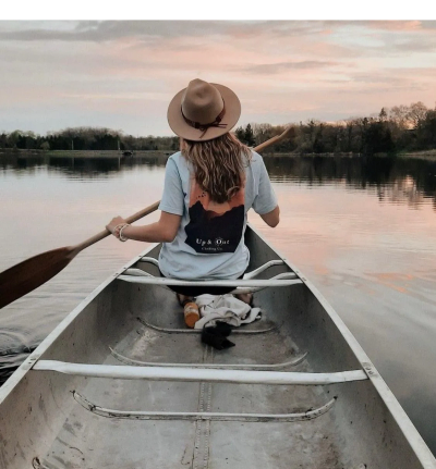 A person paddling a canoe on a calm lake during sunset.