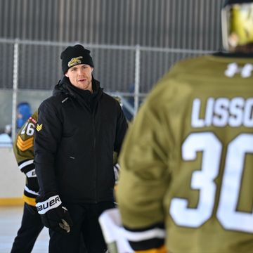 Ice hockey coach instructing players during practice on an outdoor rink.
