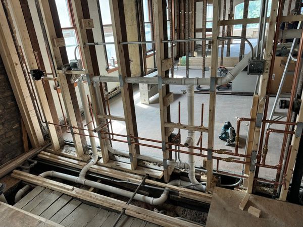 Interior view of a building under renovation showing exposed wooden framing and plumbing pipes.