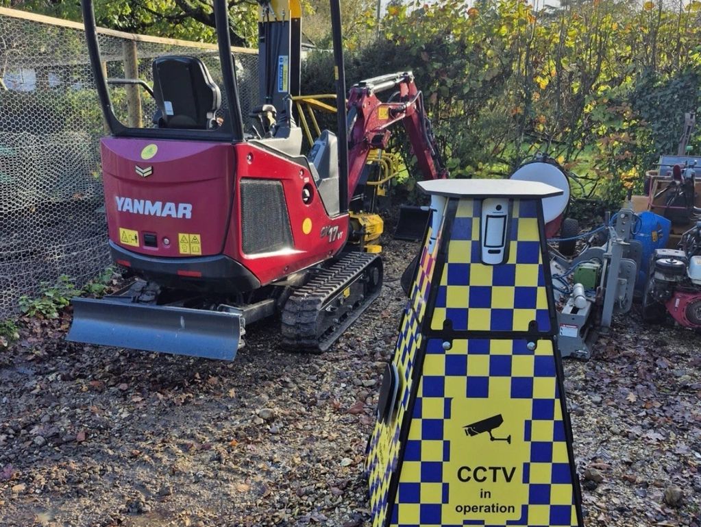 Red Yanmar excavator and surveying equipment outdoors.