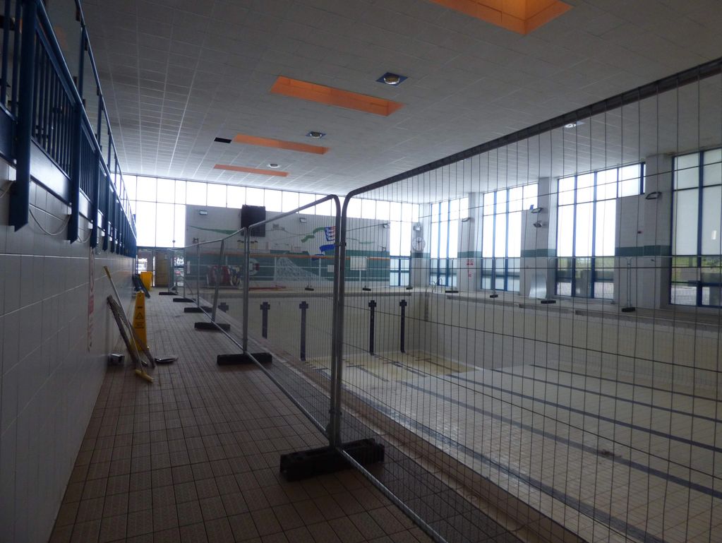 An empty indoor pool fenced off for maintenance.
