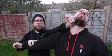 Two men demonstrating a self-defense move in a backyard.