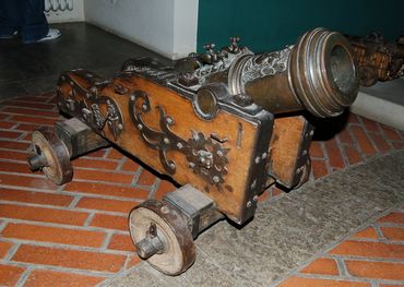 Antique small cannon with wooden wheels and ornate metal details.