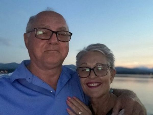 Smiling elderly couple outdoors by a lake at sunset.