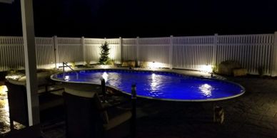 Swimming pool landscape lighting and paver patio surround with privacy fence and accent plantings by LANDDescapes, LLC Landscape Design Contractor 