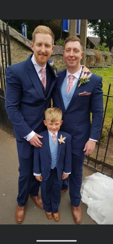 Three males in matching blue suits at an outdoor event.