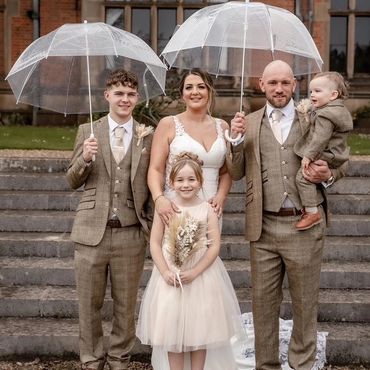Family in wedding attire holding clear umbrellas.