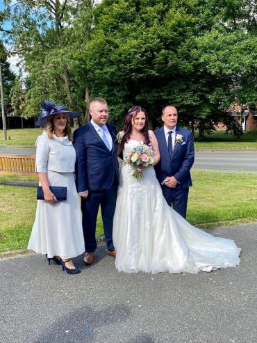 A bride and three guests posing outdoors beside a road.