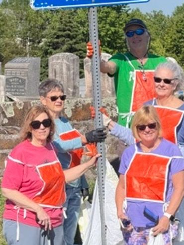 Group of adults wearing orange aprons posing outdoors near tombstones.