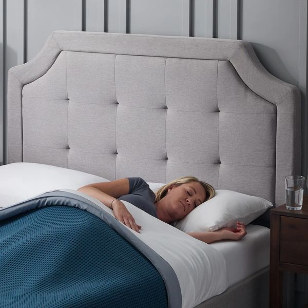 Woman peacefully sleeping in a bed with a tufted gray headboard.