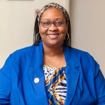 Smiling woman wearing glasses, a blue blazer, and a patterned top.