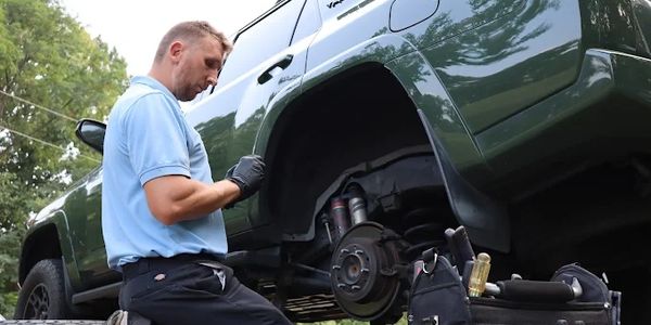 A man repairing a green SUV with the wheel removed.
