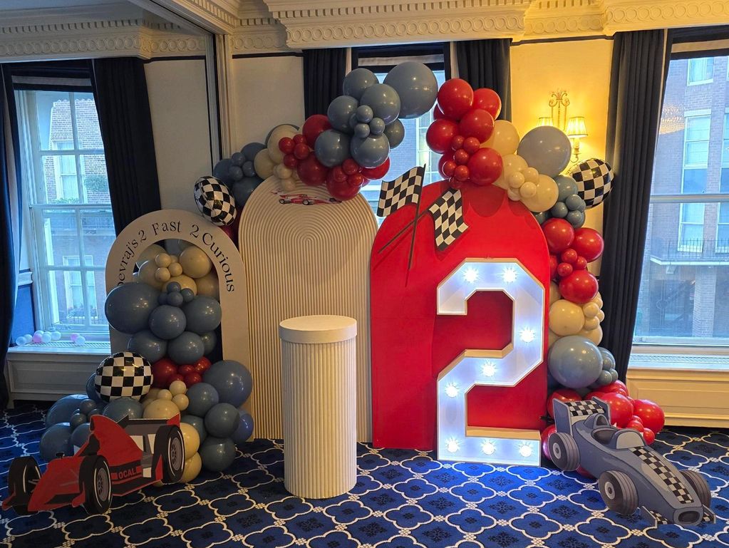 A racing-themed birthday decoration featuring balloons and a lit number 2.