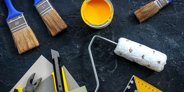 Painting tools including brushes, roller, yellow paint, and measuring tools on a dark surface.