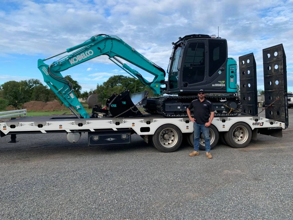 Teal 8 tonne Kobelco Excavator on trailer with man standing in front