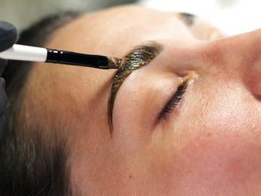 Close-up of eyebrow tinting with a brush on a woman's face.
