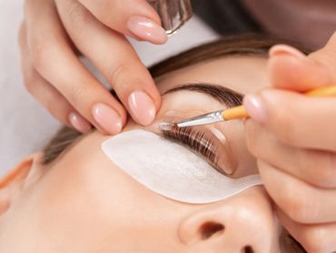 Applying eyelash extensions with precision using a small brush and adhesive.