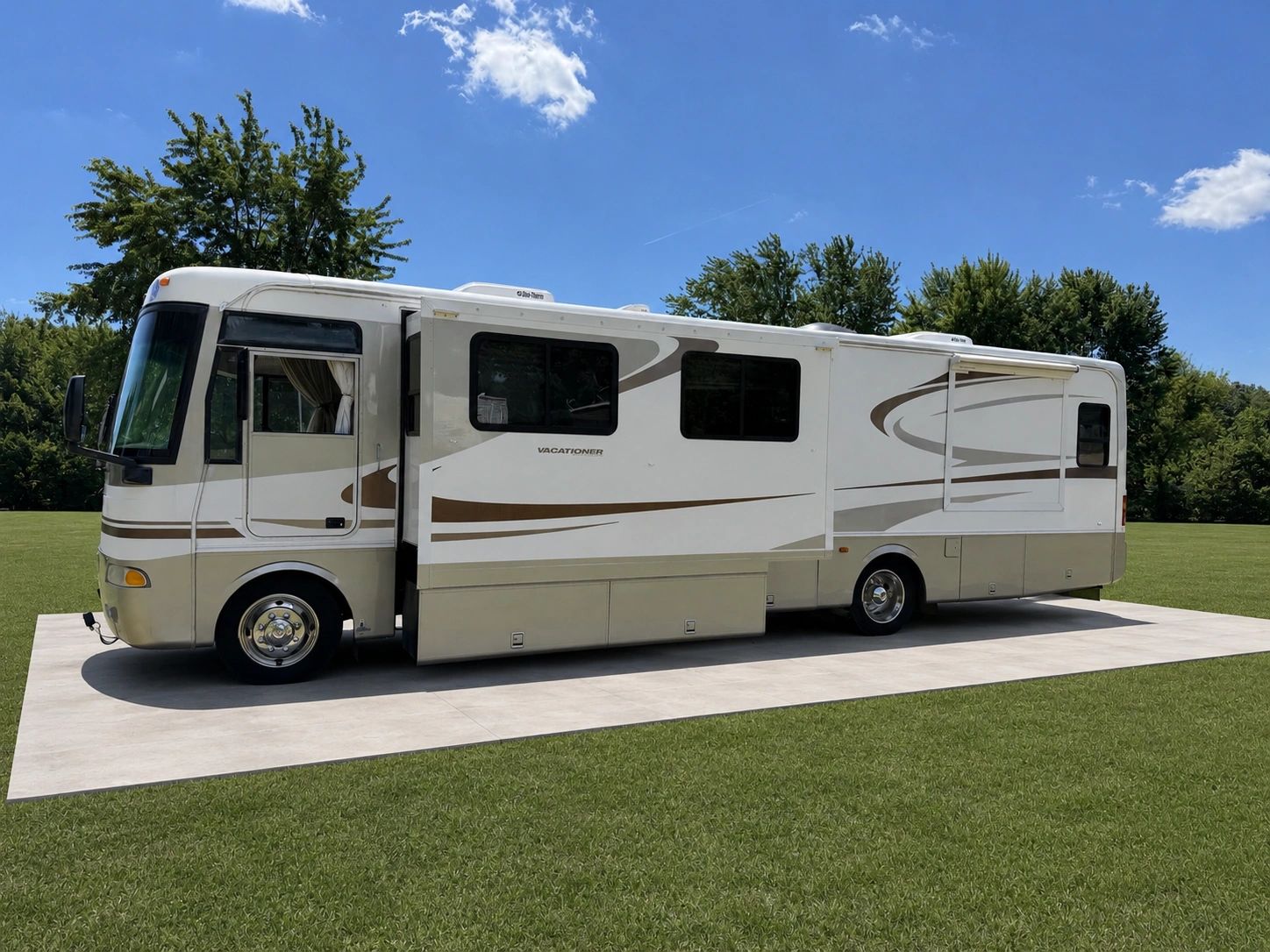 A large white and beige motorhome parked on a concrete pad in a grassy area.