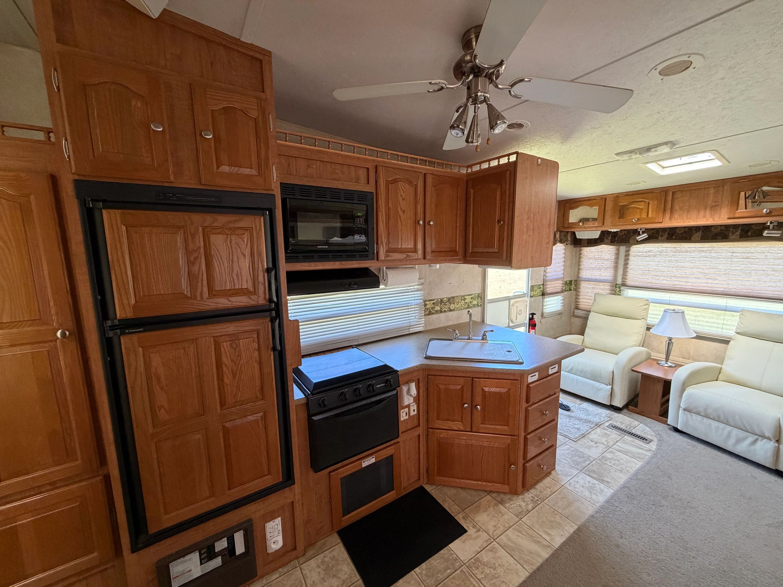 Cozy kitchen and living area inside an RV with wooden cabinetry and white leather chairs.