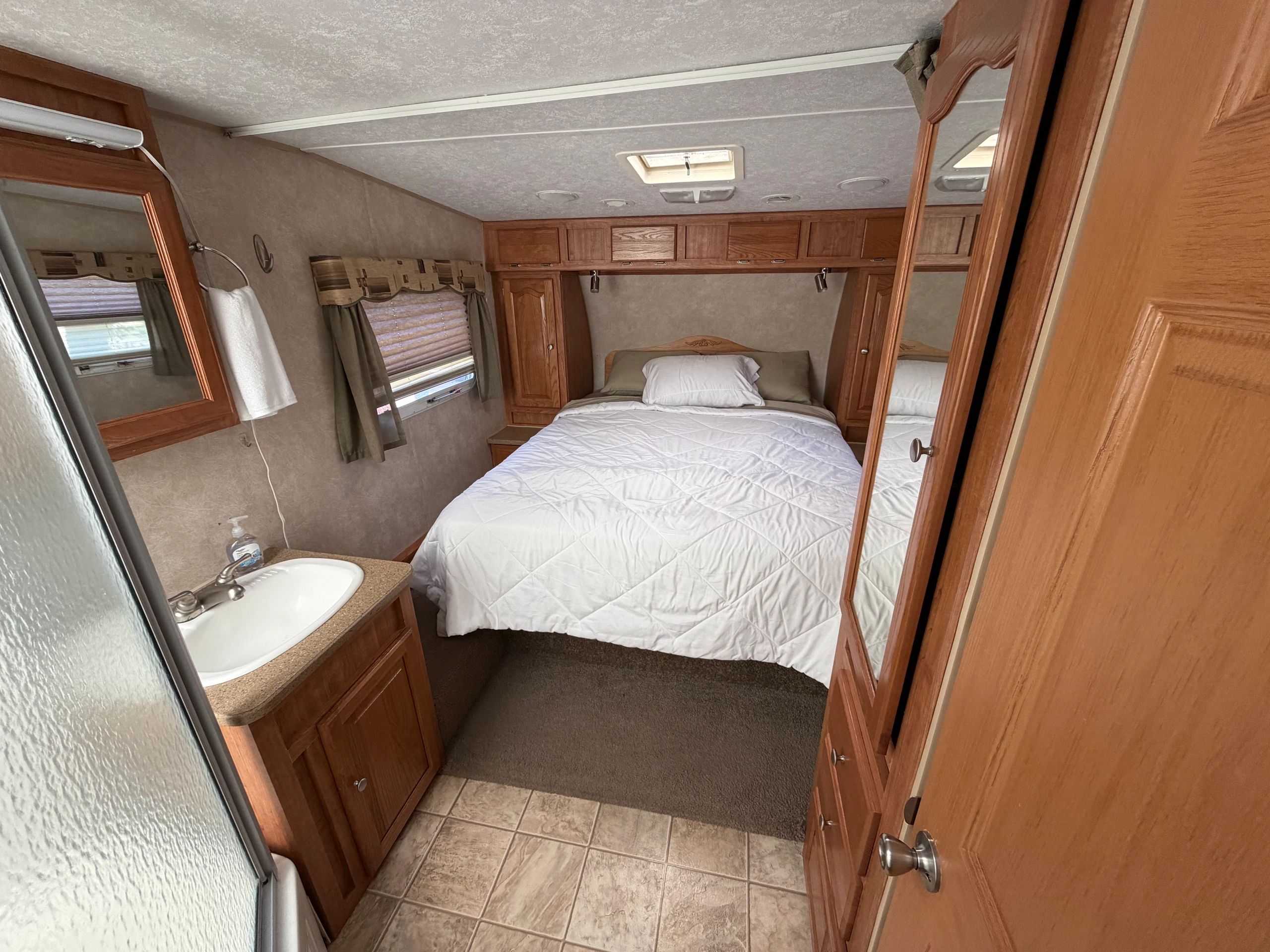 Cozy compact bedroom in an RV with wooden cabinets and a small sink.