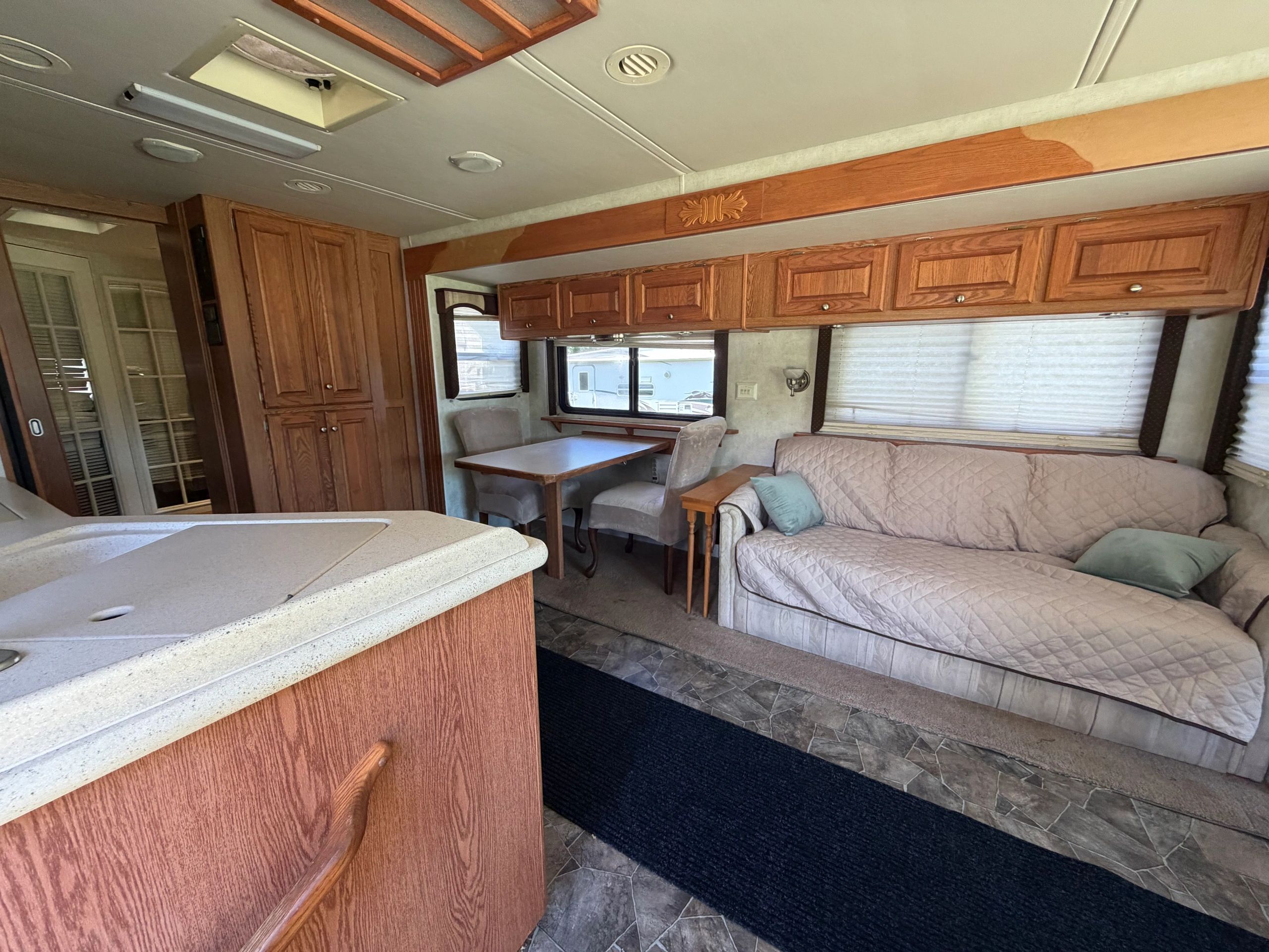 Cozy RV interior with wooden cabinets, dining area, and a covered couch.
