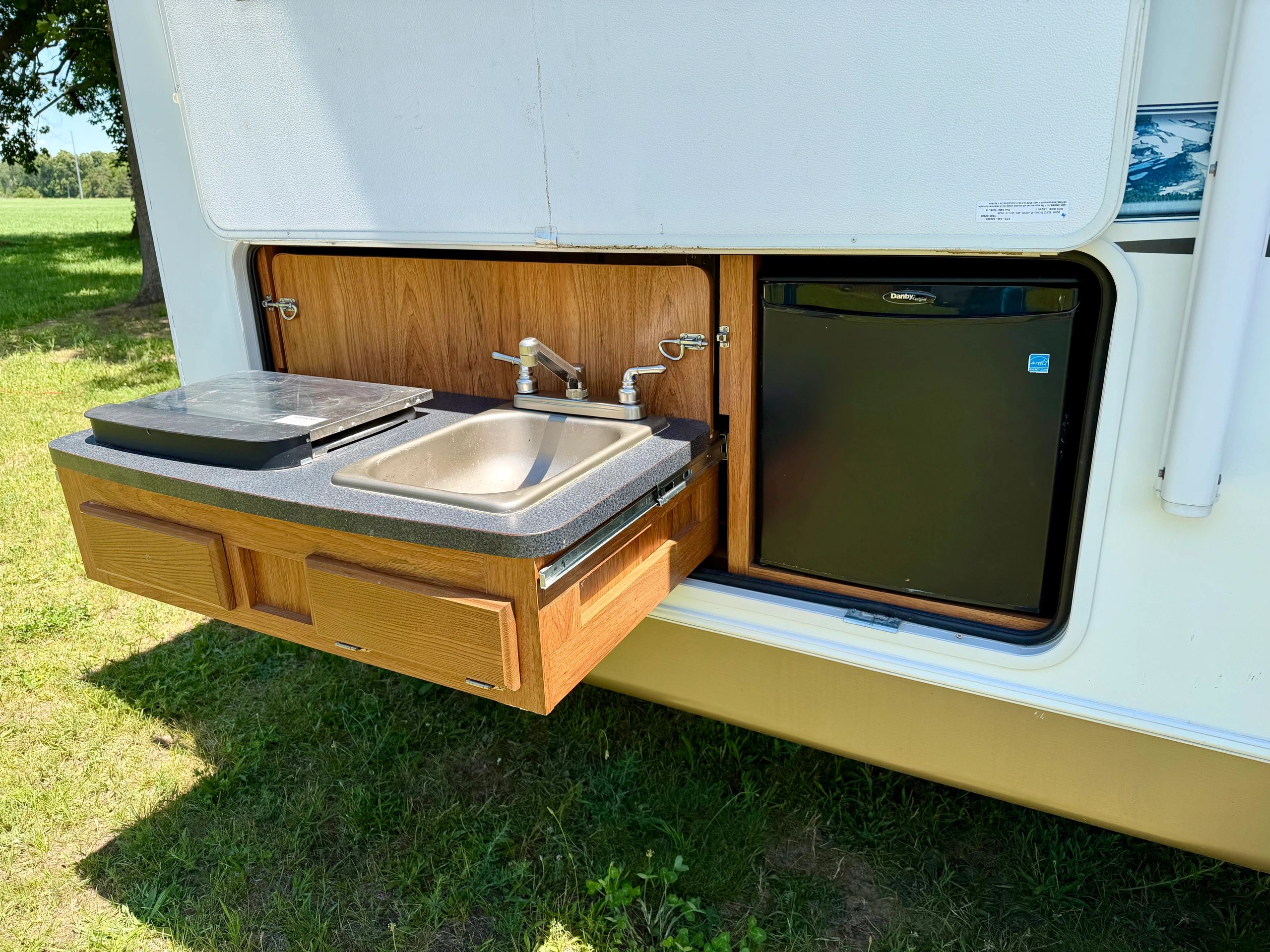 Outdoor kitchenette with sink, mini fridge, and stove in an RV setup.
