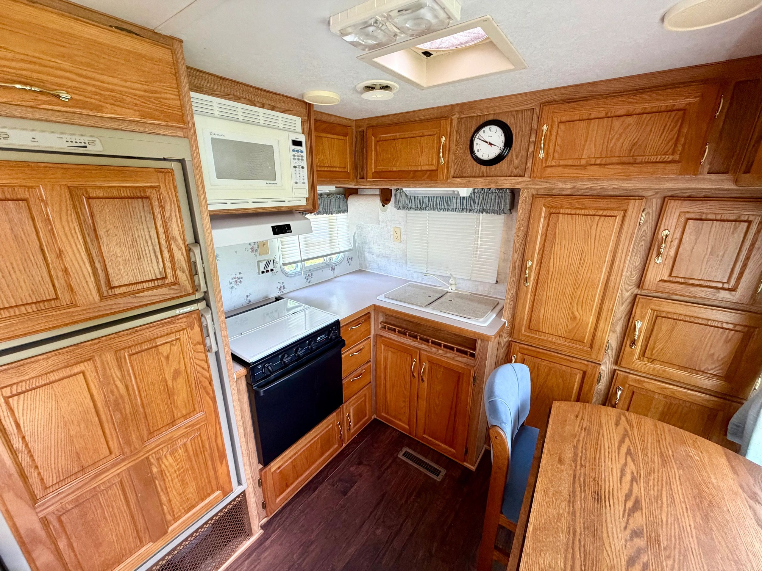 Compact wooden kitchen area with appliances inside an RV.