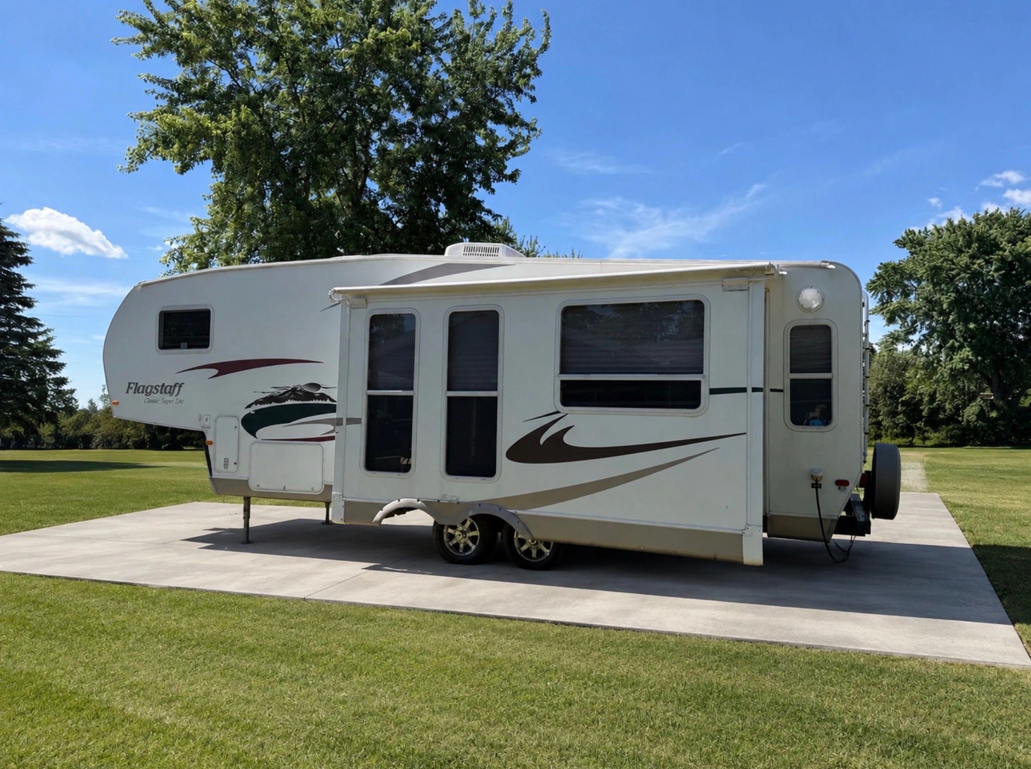 White Flagstaff fifth-wheel RV parked on a concrete pad with trees in the background.