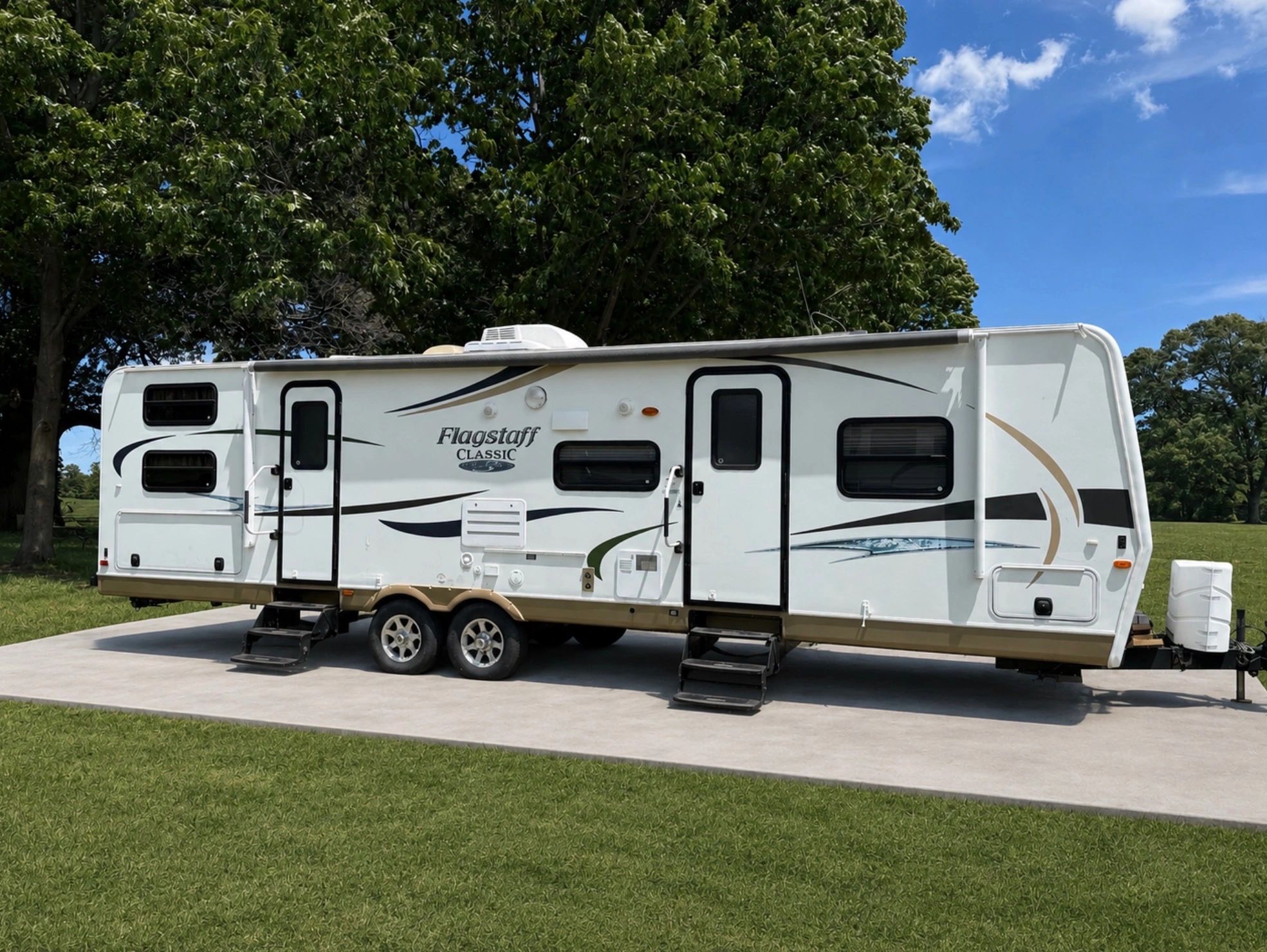 A white Flagstaff Classic RV parked on a concrete slab under green trees.