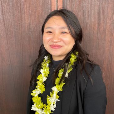 Smiling woman wearing a black blazer and a green and white flower lei.