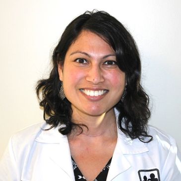 Smiling woman in a white medical coat against a plain background.