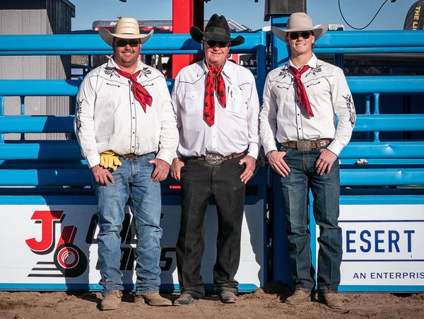 Three men in cowboy attire posing in front of a blue gate.
