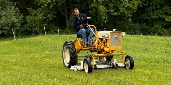 Man riding an old yellow tractor on grass.